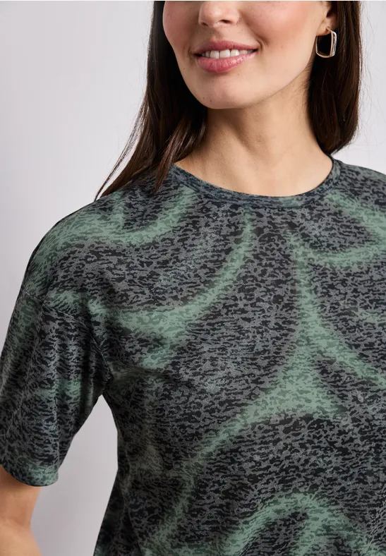 Frau in T-Shirt mit abstraktem grün-schwarzem Wirbelmuster, Nahaufnahme.