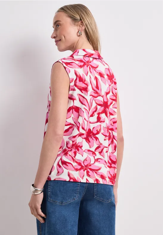 Vrouw gezien van achteren met mouwloze roze-witte top met bloemmotief en een spijkerbroek.