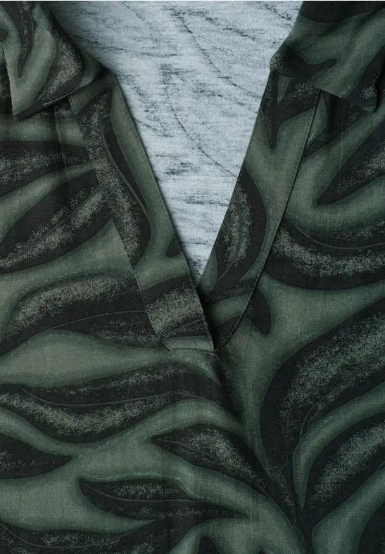 Close-up van een groene jas met abstracte, draaiende print over een grijs shirt.