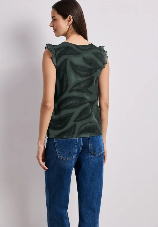 Vrouw van achteren met een groen topje met motief en een blauwe spijkerbroek.