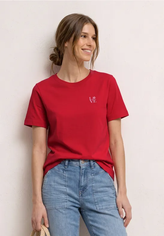 Vrouw in rood T-shirt en blauwe spijkerbroek tegen neutrale achtergrond