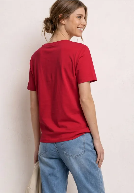 Vrouw van achteren met rood T-shirt, korte mouwen en blauwe jeans, haren los in knot
