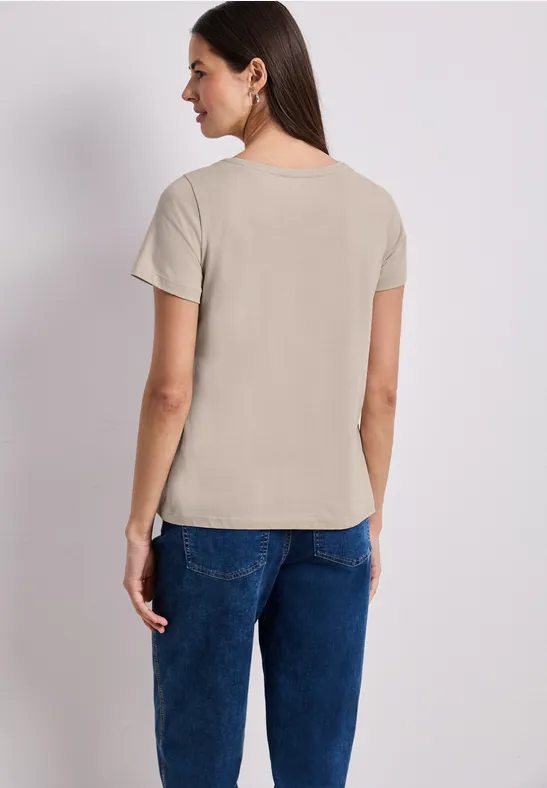 Een vrouw van achteren in een beige t-shirt en een blauwe spijkerbroek tegen een witte achtergrond.