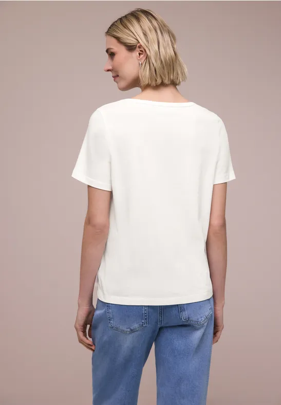 Vrouw van achteren in een wit T-shirt en blauwe jeans voor een neutrale achtergrond.