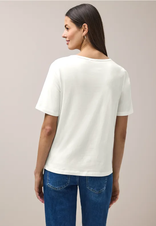 Person von hinten in weißem T-Shirt und blauen Jeans vor neutralem Hintergrund.