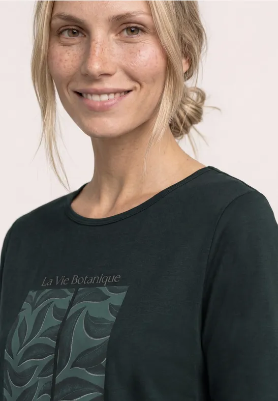 Een vrouw draagt een zwart T-shirt met botanisch motief en de tekst "La Vie Botanique".