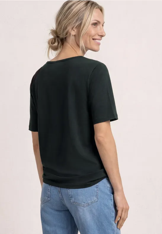 Vrouw van achteren met zwart T-shirt en spijkerbroek, blonde haren in een losse knot.