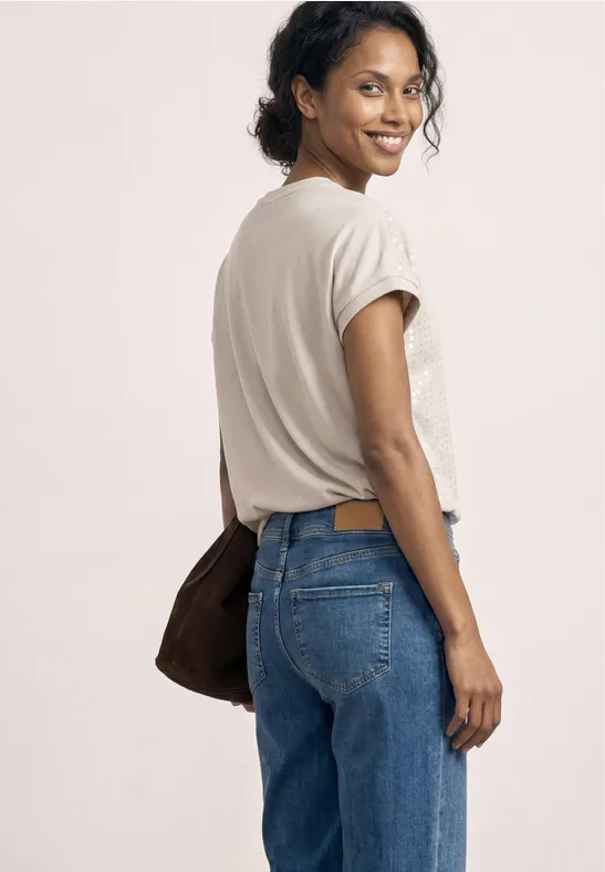 Femme en t-shirt blanc, jean bleu et sac, regard par-dessus l’épaule.