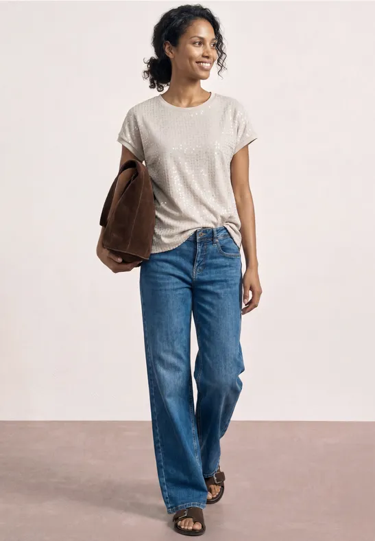 Personne en t-shirt blanc, jean bleu et sandales, tenant une veste marron sous le bras.