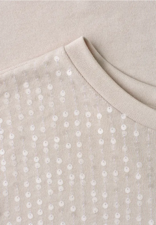 Pull beige à col rond orné de paillettes brillantes disposées en rangées sur le devant.