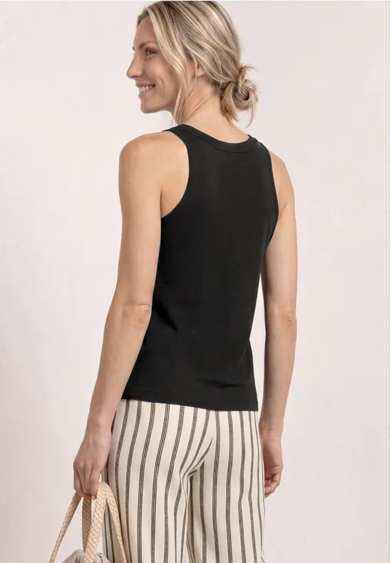 Vrouw van achter gezien met zwarte top, wit-zwart gestreepte broek en een strooien tas in haar hand.