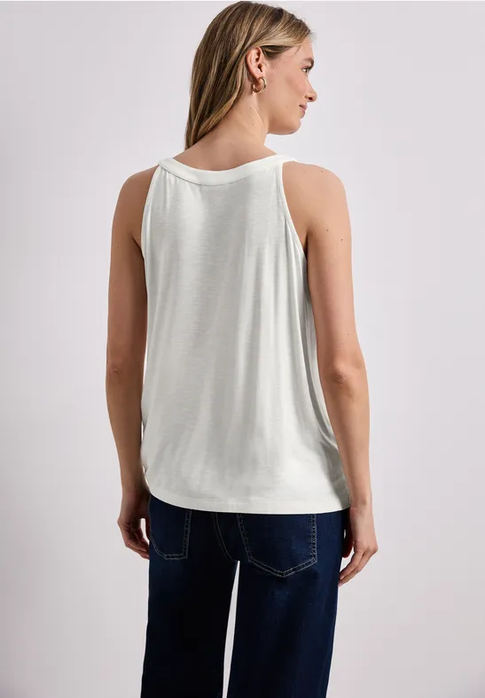 Vrouw van achteren in een wit mouwloos shirt en blauwe spijkerbroek voor een lichte achtergrond.