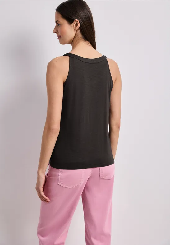 Vrouw, rugzicht, draagt zwart mouwloos top en roze broek voor lichte achtergrond.