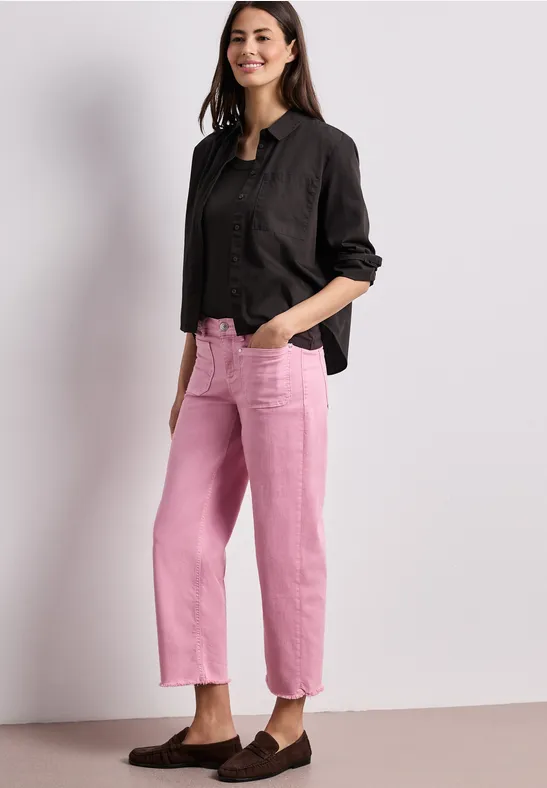 Iemand draagt een zwart overhemd en roze rechte broek tegen een eenvoudige achtergrond.