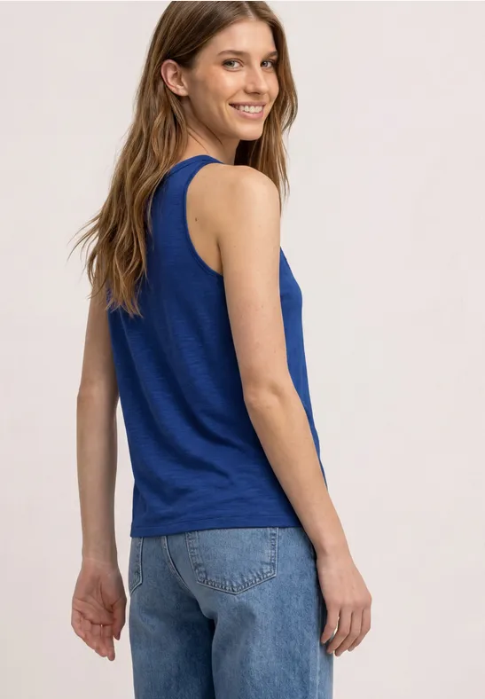 Frau von hinten in blauem ärmellosem Top und Jeans vor hellem Hintergrund.