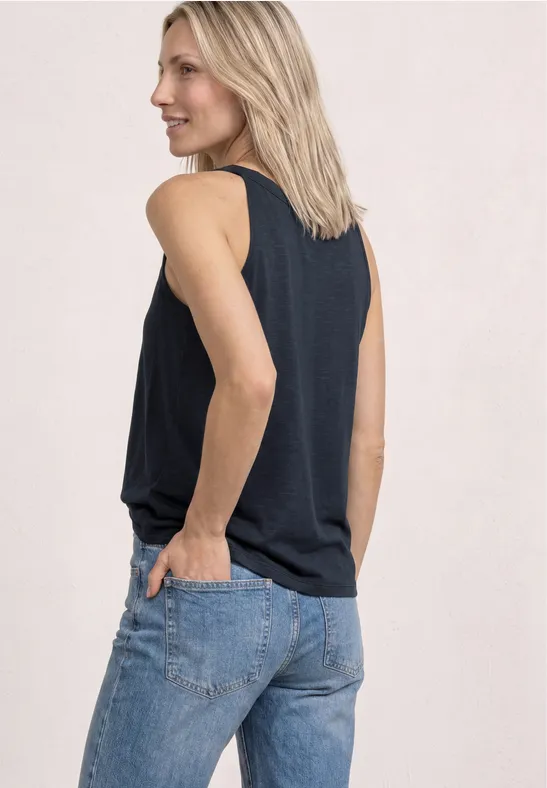 Een persoon van achteren in een mouwloos topje en jeans, handen in de achterzakken.