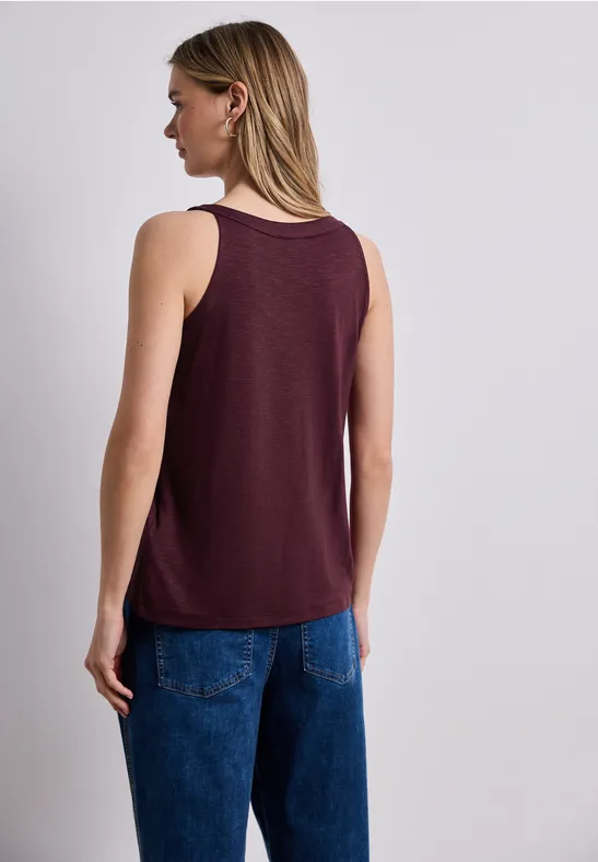 Vrouw van achteren in een bordeaux tanktop en blauwe jeans, halflang blond haar.