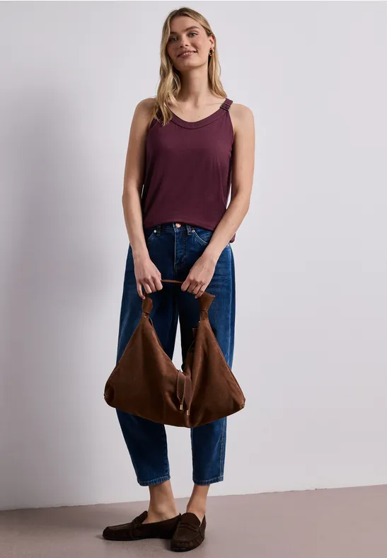 Vrouw in losse jeans en top houdt een bruine tas vast.