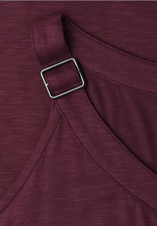 Close-up van een bordeaux kledingstuk met verstelbare band en vierkante metalen gesp.