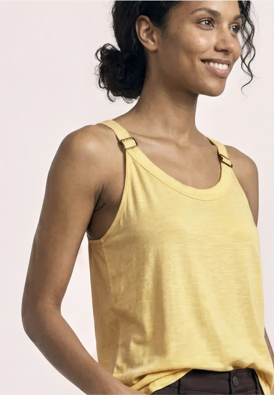 Persoon in gele mouwloze top, close-up van schouders en bovenlijf, met krullend haar.