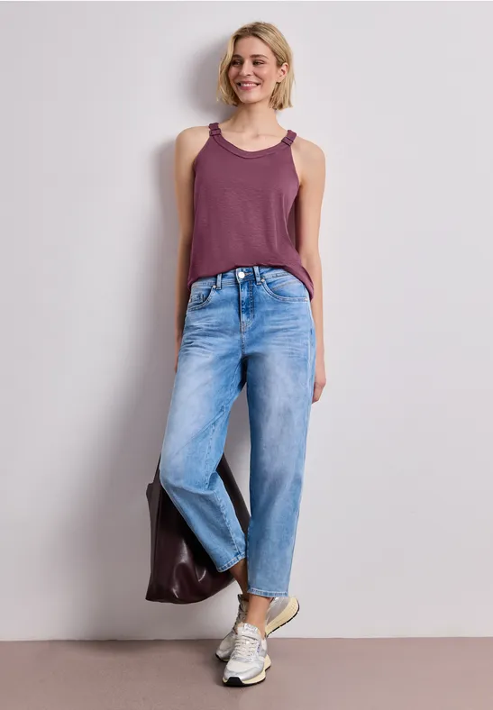 Eine Frau in einem lila Top, weiten Jeans und weißen Sneakern trägt eine braune Tasche.