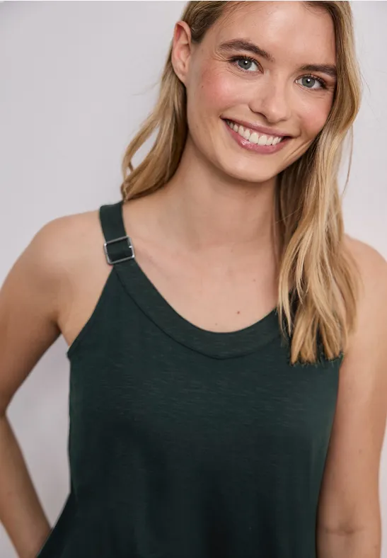 Vrouw met lang blond haar draagt een donker mouwloos hemd tegen een neutrale achtergrond.