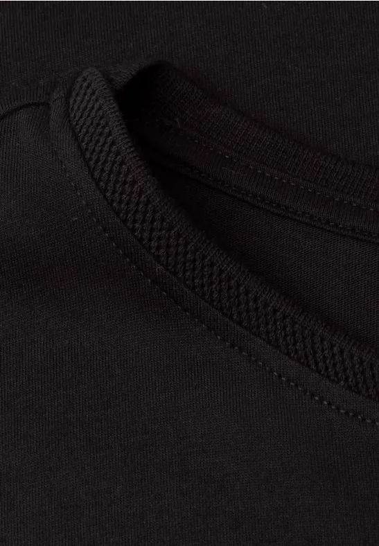 Close-up van een zwart T-shirt met ronde hals en duidelijke, nette naad.