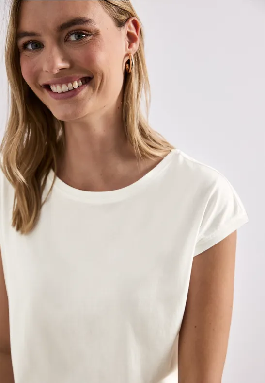 Jonge vrouw glimlacht in wit T-shirt, halflang blond haar, oorbellen, heldere studiofoto.