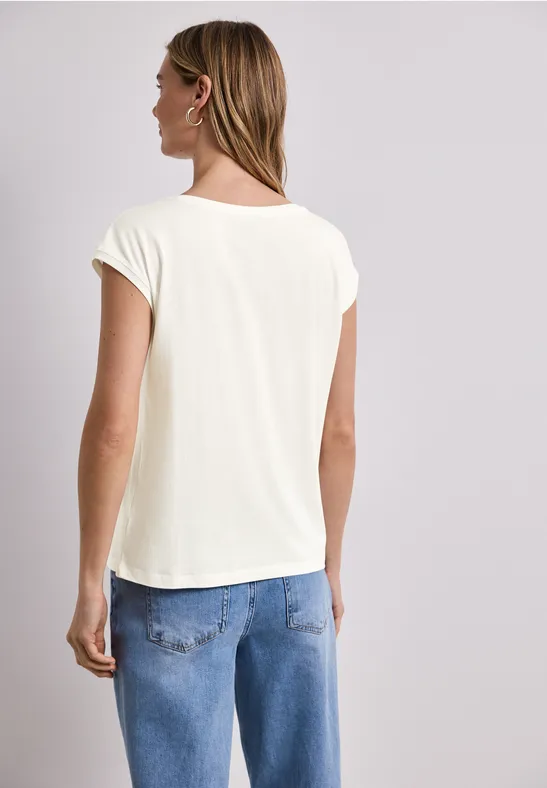 Vrouw met blond haar draagt een wit t-shirt en blauwe jeans, gezien van achteren.