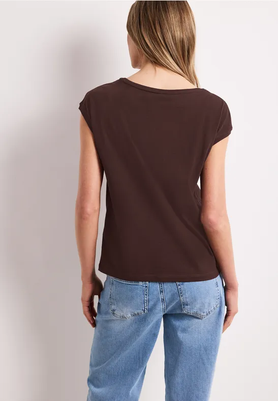 Femme de dos portant un haut marron et un jean bleu clair devant un fond blanc.