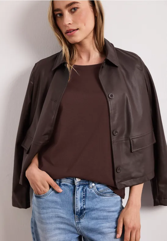 Femme porte une veste en cuir marron sur un t-shirt brun foncé et un jean bleu clair.