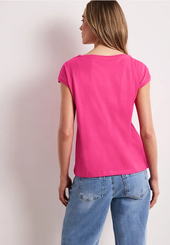 Een vrouw gezien van achteren in een roze shirt en blauwe spijkerbroek.
