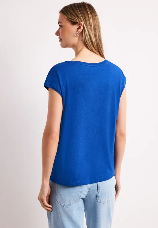 Vrouw van achteren in een koningsblauw T-shirt met korte mouwen en lichte jeans voor een witte achtergrond.