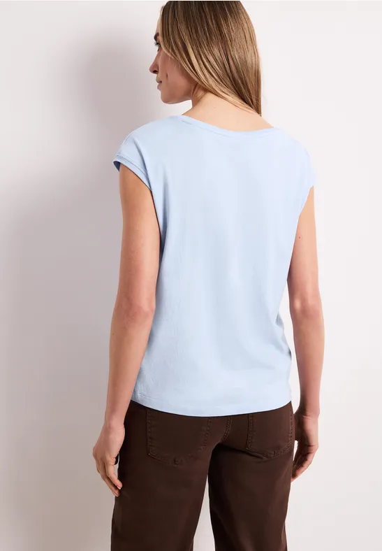 Vrouw van achteren met lichtblauw t-shirt en bruine broek.