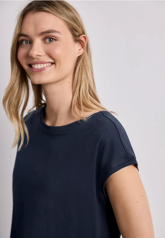 Een vrouw in een marineblauw T-shirt voor een lichte achtergrond, gezicht vervaagd