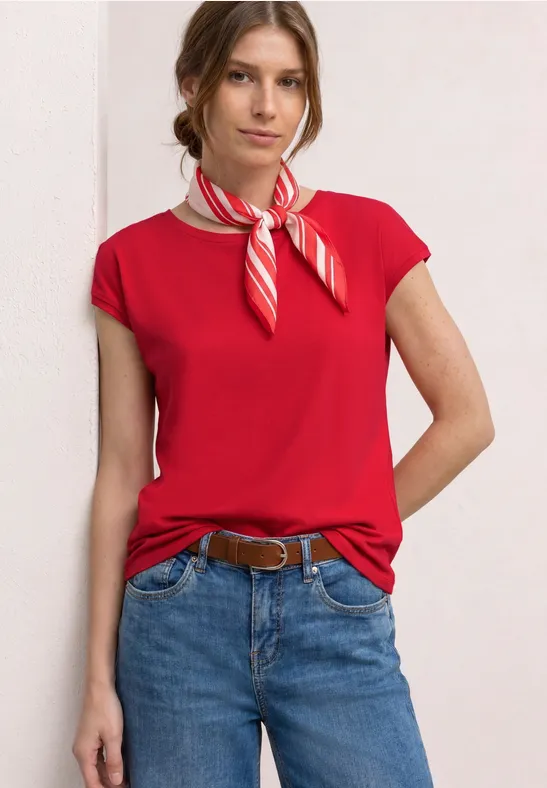 Vrouw in rood t-shirt, spijkerbroek, riem en rood-wit gestreept sjaaltje.