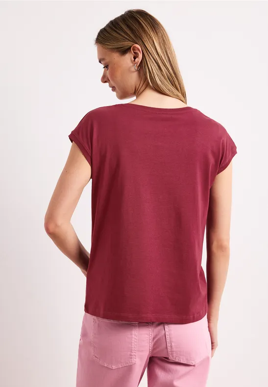 Vrouw van achteren in een bordeauxrood T-shirt en roze jeans voor witte achtergrond.