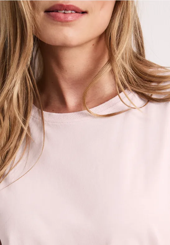 Close-up van een blonde vrouw in een roze T-shirt, enkel de hals en lippen zichtbaar.