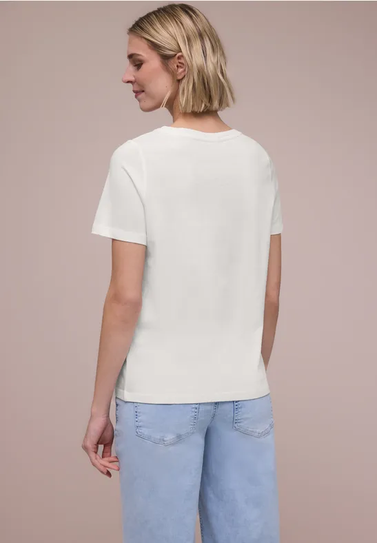 Een vrouw met kort blond haar draagt een wit T-shirt en blauwe spijkerbroek, gezien van achteren.