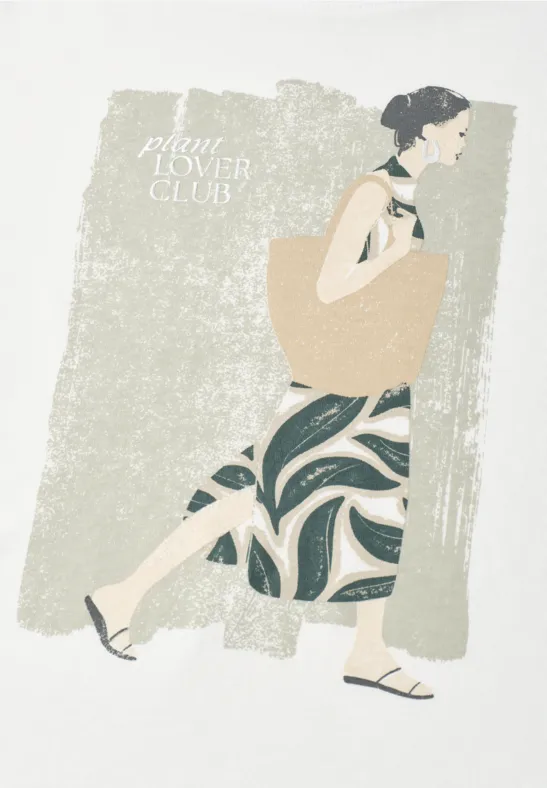 Vrouw in jurk met patroon en grote tas, lopend tegen een beige, getextureerde achtergrond.