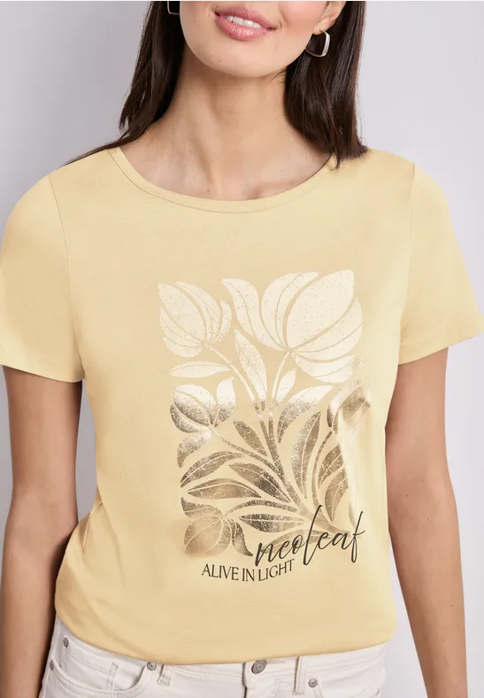 Vrouw draagt geel t-shirt met bladmotief en opschrift