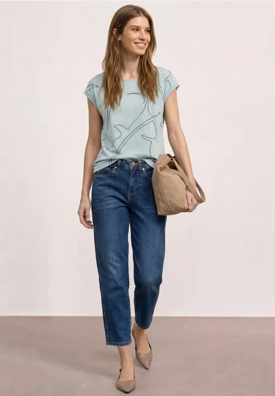 Jonge vrouw in een casual look: lichtblauw ster-T-shirt, rechte jeans, platte schoenen en een canvas tas.