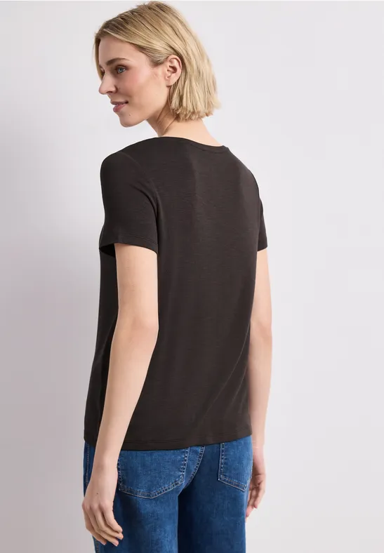 Achteraanzicht van een vrouw met kort blond haar, zwarte t-shirt en blauwe jeans.