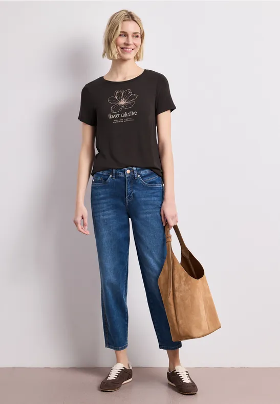 Vrouw in zwart T-shirt en blauwe jeans met cognackleurige stoffen tas.