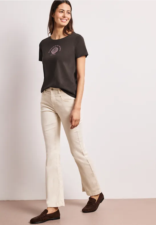 Kobieta w czarnym t-shircie i kremowych dzwonach, pozująca na jasnym tle.