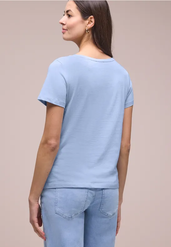 Vrouw van achteren in lichtblauw T-shirt en spijkerbroek voor neutrale achtergrond.