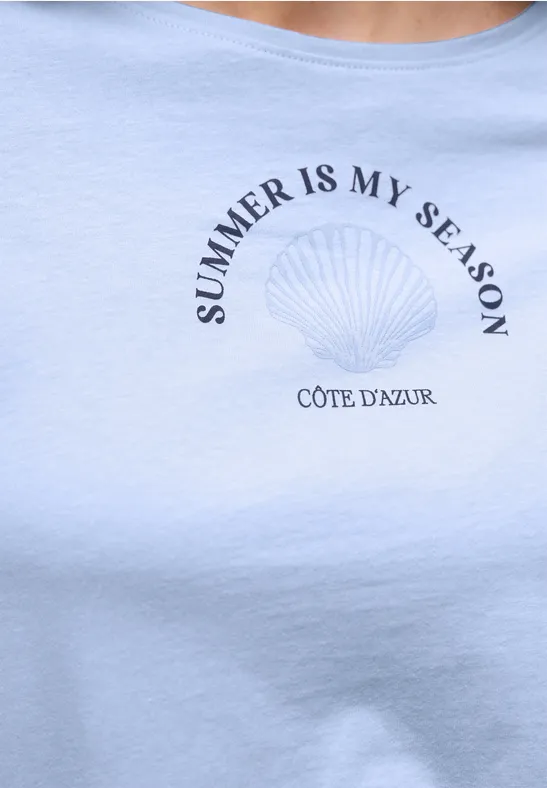 Lichtblauw T-shirt met schelpmotief en tekst "SUMMER IS MY SEASON" en "CÔTE D'AZUR".