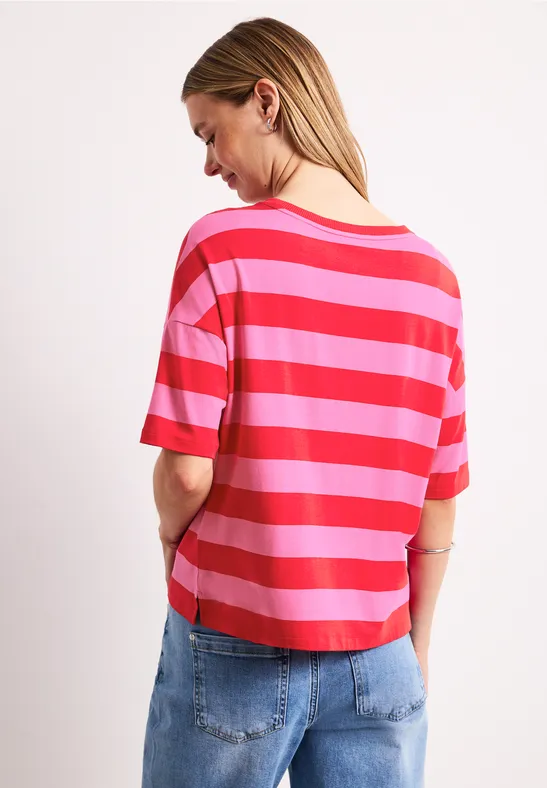 Vrouw van achteren met rood-roze gestreept t-shirt en blauwe jeans voor een witte achtergrond.