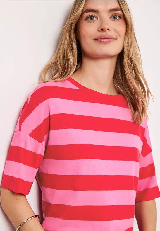 Jonge vrouw lacht, draagt roze-rood gestreept T-shirt met korte mouwen tegen lichte achtergrond.