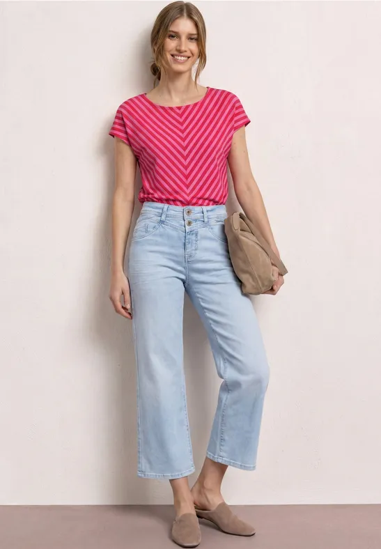 Vrouw in roze gestreept T-shirt, lichtblauwe wijde jeans, schoudertas en beige loafers.